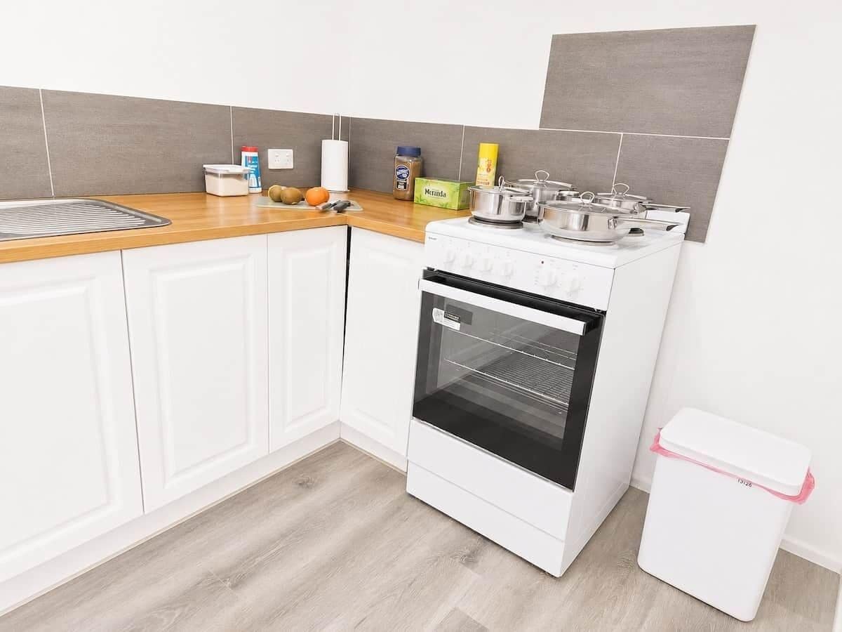 Een keuken met witte kasten, een houten aanrechtblad, een witte oven en een vuilnisbak.