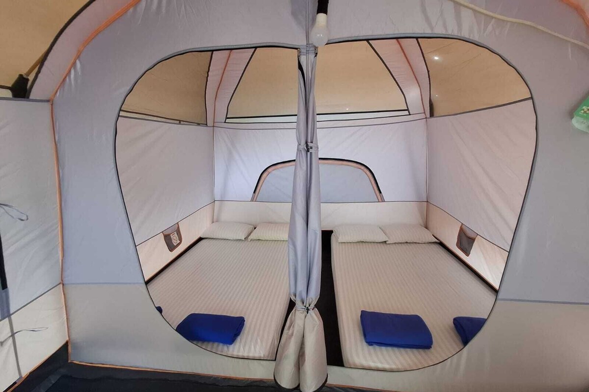 A tent with a circular entrance, two beds with blue pillows, and a central pole.