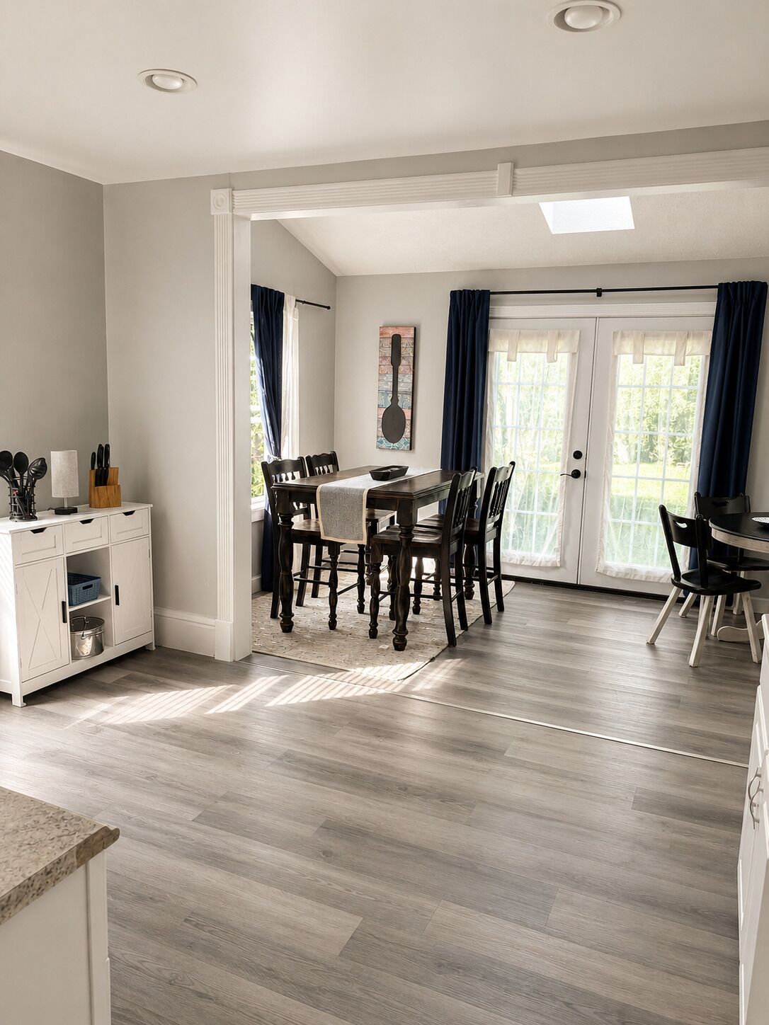 A dining area with a table and chairs, a kitchen area with cabinets, and a view through a glass door.