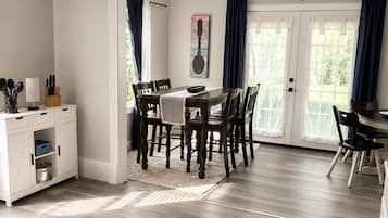 A dining area with a table and chairs, a kitchen area with cabinets, and a view through a glass door.