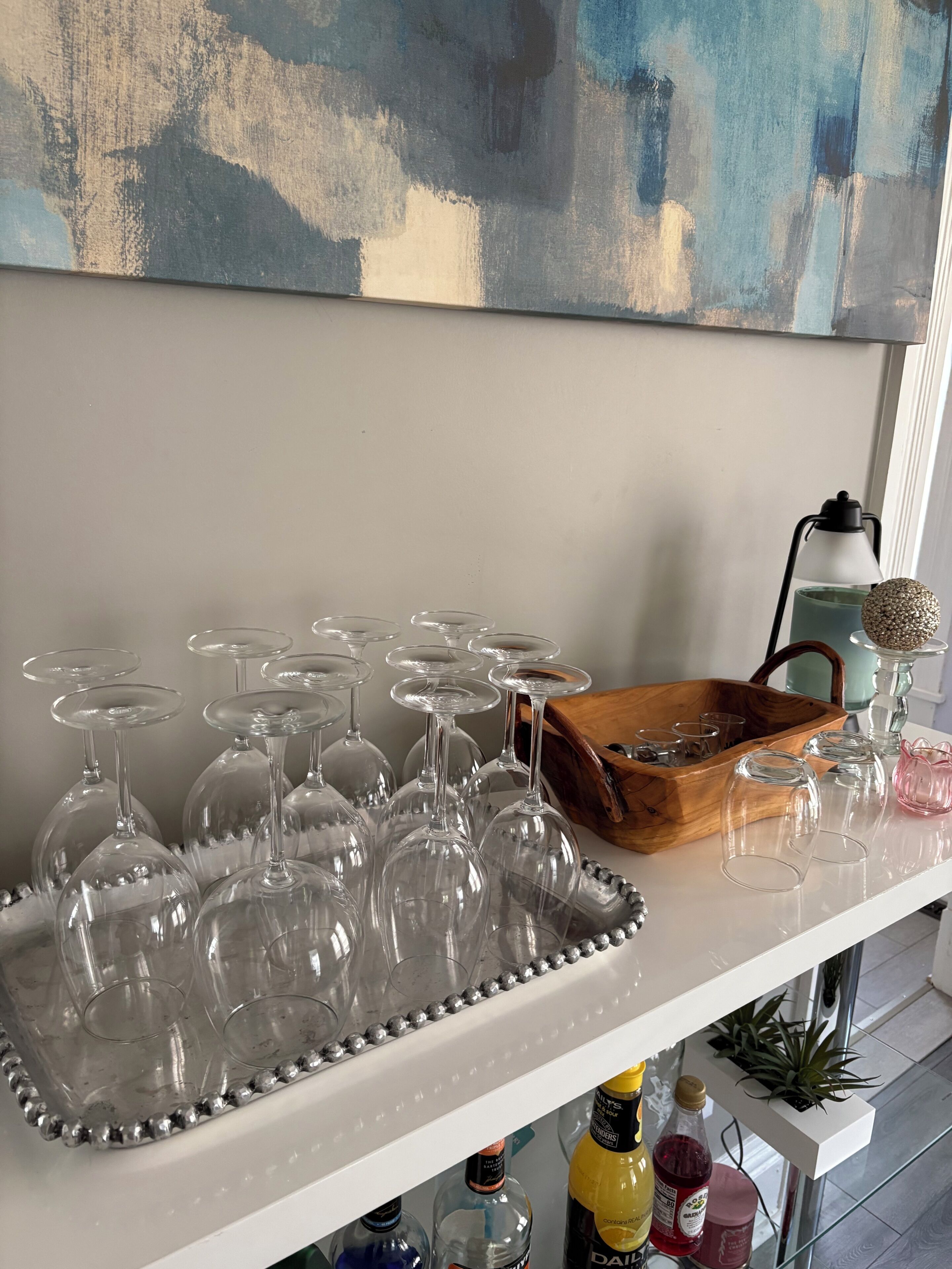 Un coin bar avec un plateau de verres à vin, un panier en bois et des bouteilles de boissons.