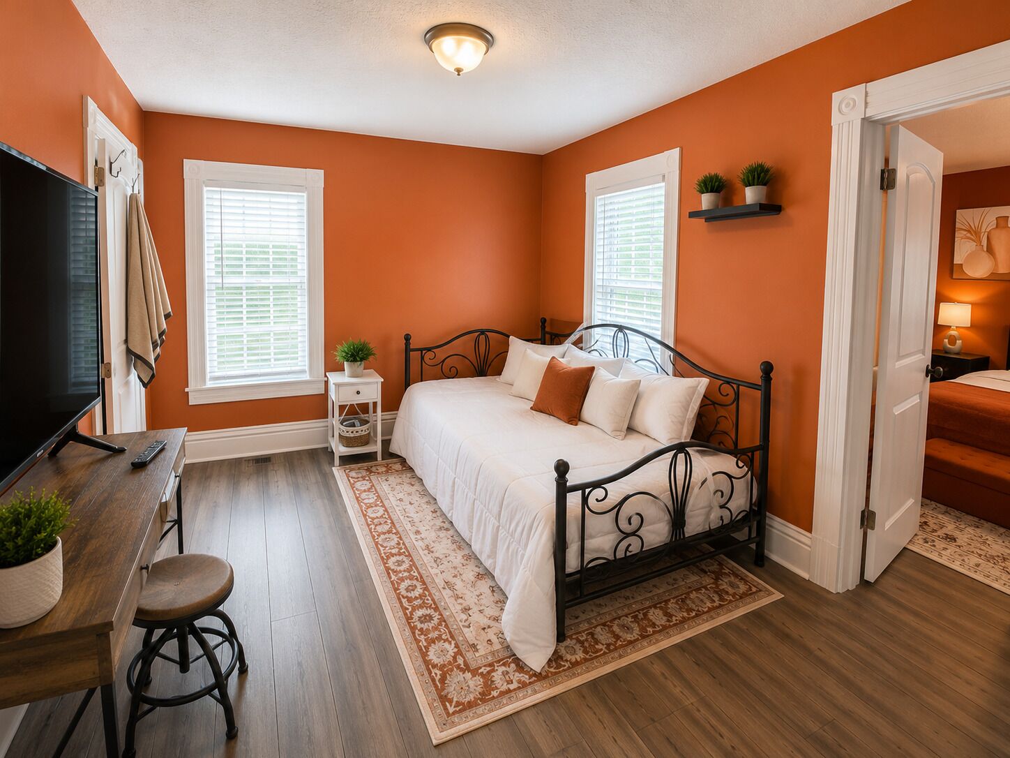 A bedroom with a bed, a desk with a TV, and two windows with blinds.