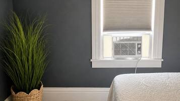 Et værelse med mørk væg, et vindue med skodder, en radiator, en potteplante og en seng med et mønstret sengetæppe.