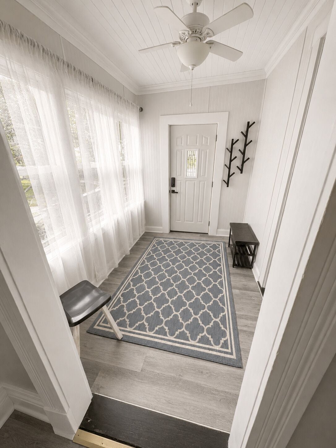 A hallway with a patterned rug, a bench, a door, and a ceiling fan.