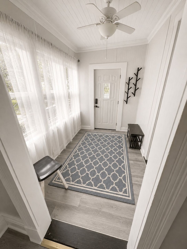 A hallway with a patterned rug, a bench, a door, and a ceiling fan.
