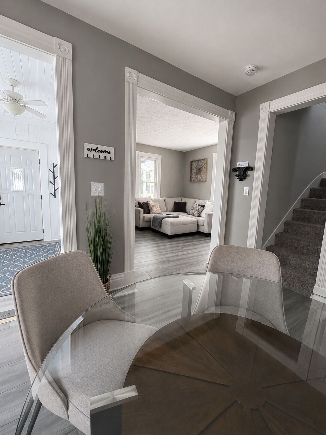 A modern living room with a glass coffee table, two chairs, a sofa, and a staircase.