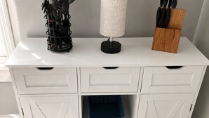 Un meuble de cuisine blanc, avec une casserole en métal, un panier bleu et un porte-ustensiles noir.