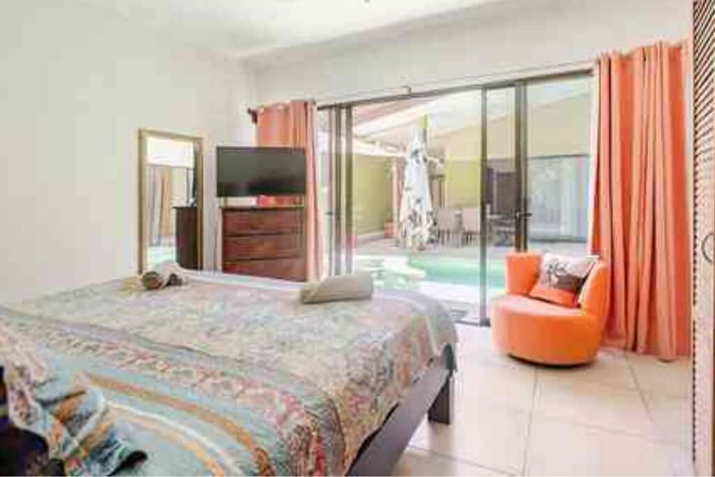 A bedroom with a bed, a television, and a sliding glass door leading to a balcony with a chair.