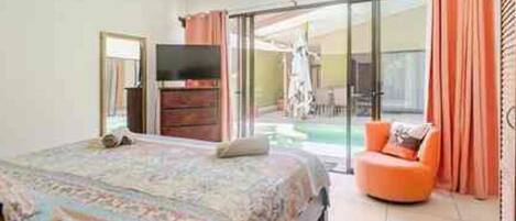 A bedroom with a bed, a television, and a sliding glass door leading to a balcony with a chair.