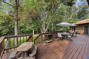 Eine Holzterrasse mit Gartenmöbeln, einem Grill und einem überdachten Tisch mit Stühlen.