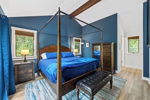 Ein Bett mit Baldachin, ein Holzgestell, eine Bank und eine Kommode in einem Zimmer mit blauen Wänden und Holzboden.