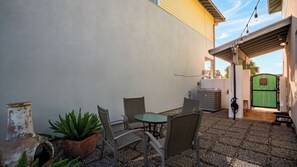 Eine Terrasse im Freien mit Tisch, Stühlen, einem Blumentopf und einem grünen Tor.