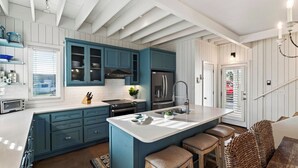 Una cocina con gabinetes color turquesa, encimera blanca y una isla central con taburetes.