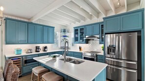 A modern kitchen with teal cabinets, stainless steel appliances, and a central island with a sink. - Chasing Sunshine by Avantstay Shared Pool + Gazebo + Covered Patio Walk to the Beach (Port Aransas)