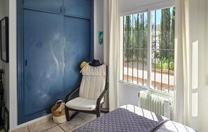 Ein Schlafzimmer mit einem Bett, einem Sessel, einem Fenster mit Blick auf Grünflächen und einem blauen Kleiderschrank.
