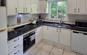 A kitchen with white cabinets, a black countertop, a sink, a microwave, and a window with a view of greenery. - Cozy home in Viñuela with private swimming pool, can be inside or outside (Viñuela)