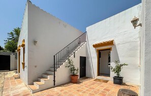 A white building with a staircase leading to a door, potted plants, and a tiled patio area. - Cozy home in Viñuela with private swimming pool, can be inside or outside (Viñuela)