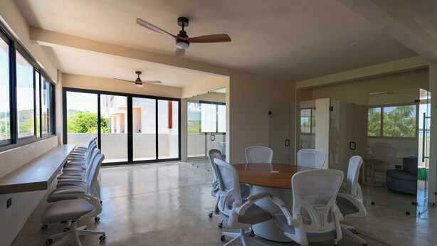 Une salle de conférence avec une longue table, des chaises blanches et un ventilateur de plafond.