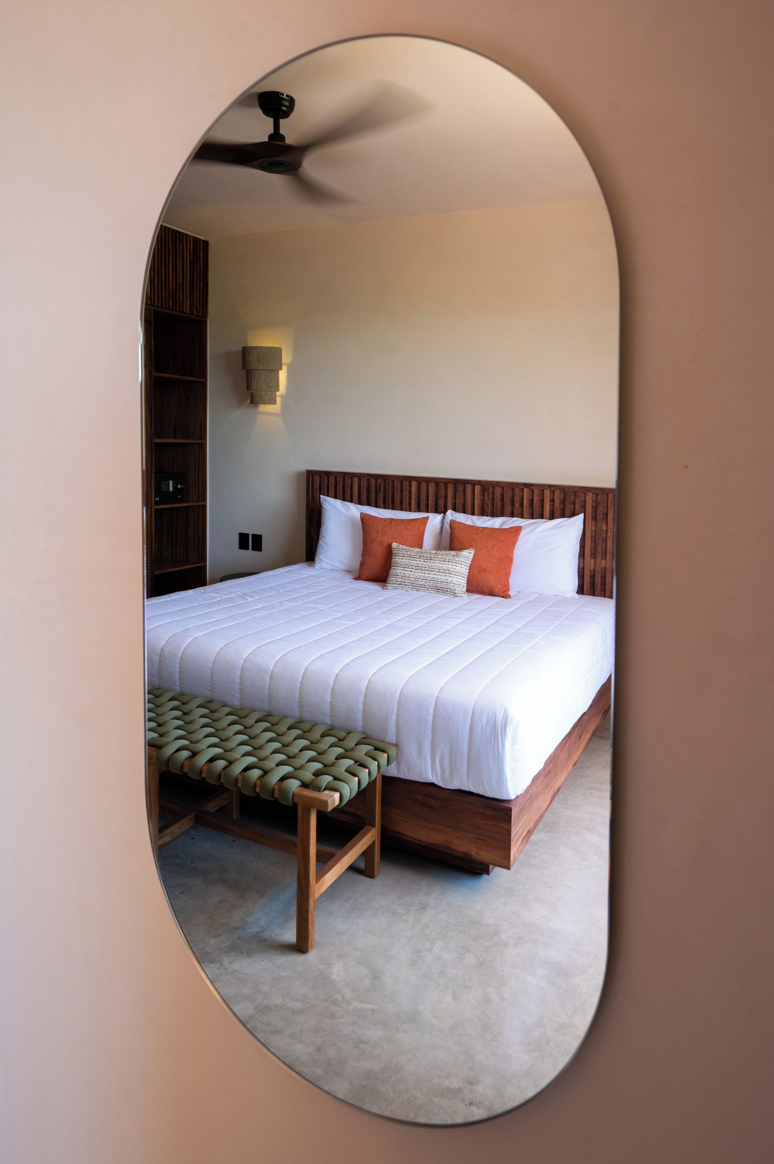 Un dormitorio con una cama grande, cabecera de madera, un banco al pie de la cama y un ventilador de techo.