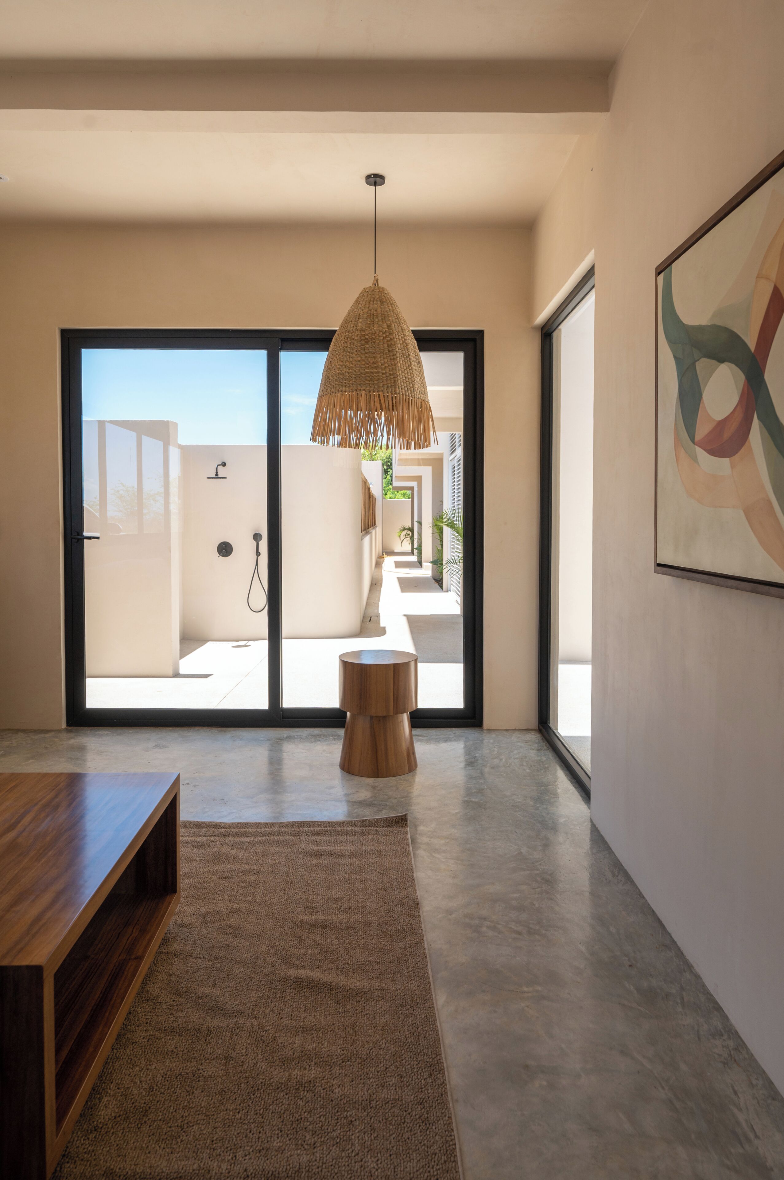 Un interior moderno con un amplio ventanal corredero que da a un espacio exterior, una lámpara colgante de fibra natural y un banco de madera minimalista.