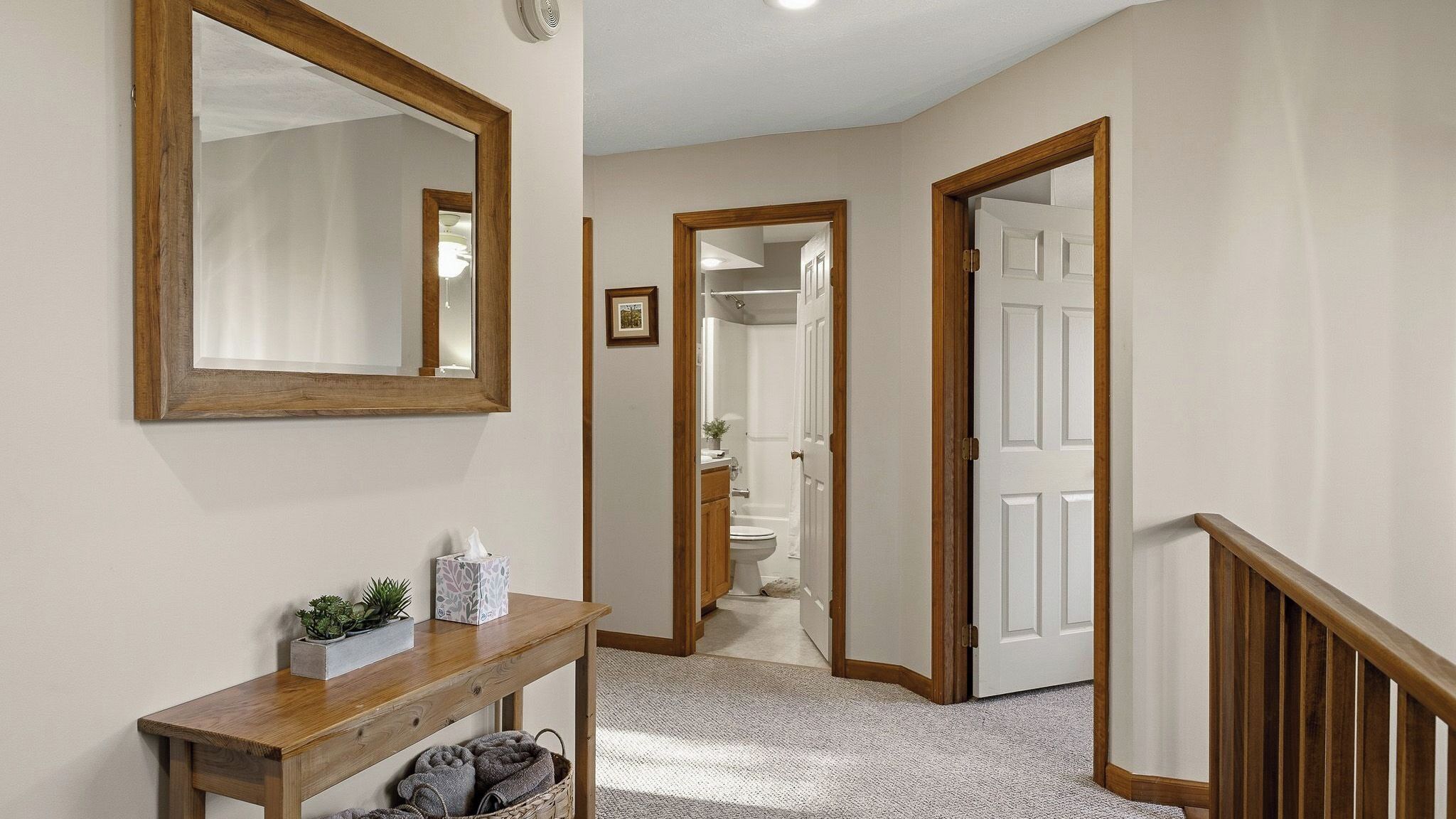 A hallway with a wooden console table, a mirror, and a door leading to a bathroom.