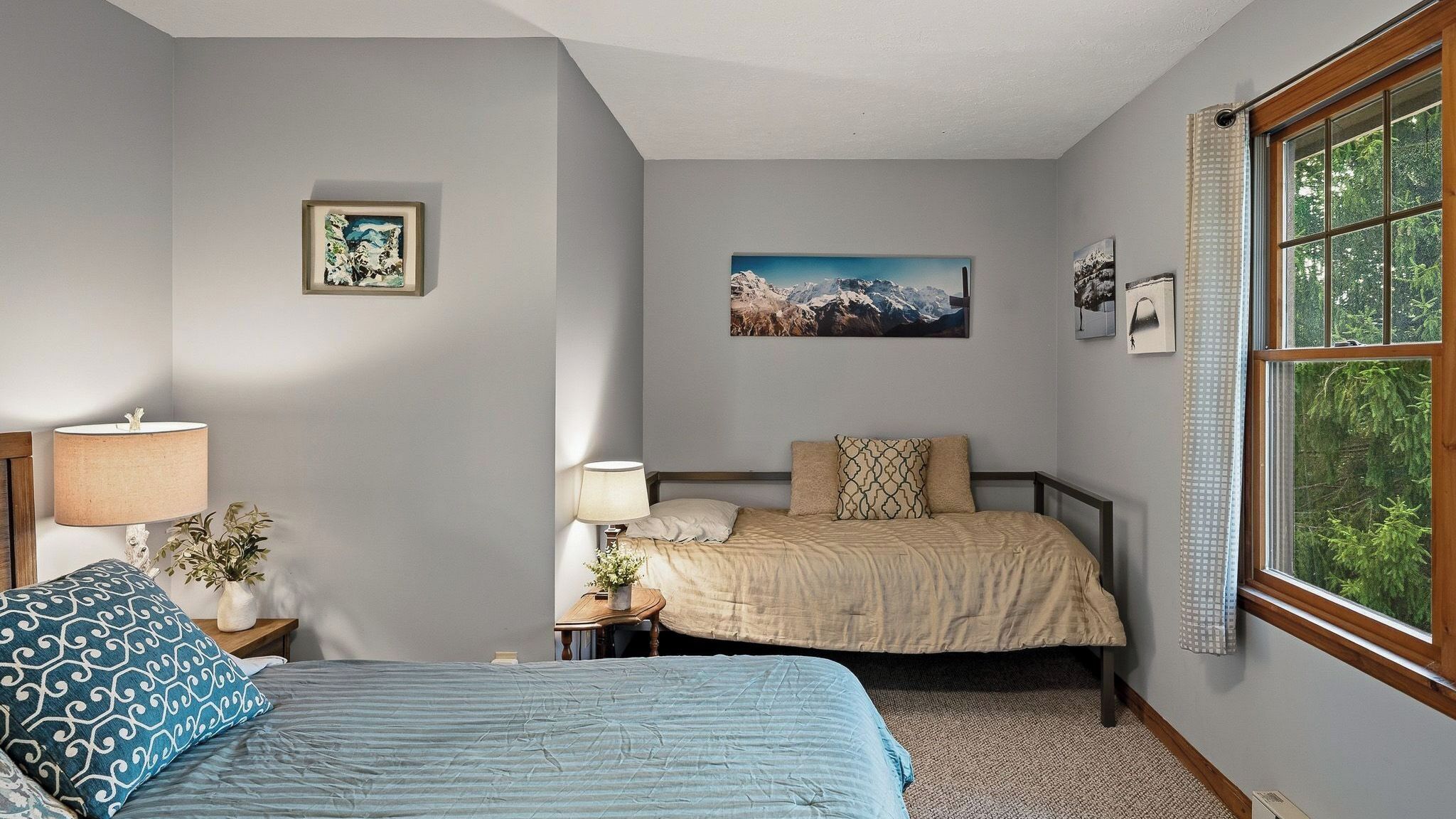 A bedroom with two beds, a window with a view of greenery, and artwork on the walls.