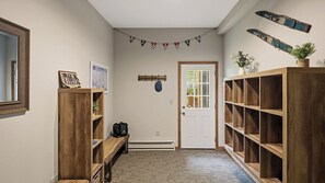 A hallway with wooden bookshelves, a bench, a coat rack, and a door with a window. - Aspen Hollow by Avantstay Group-friendly Stay + Deck Dining + BBQ Near Ski + Waterparks (Tannersville)