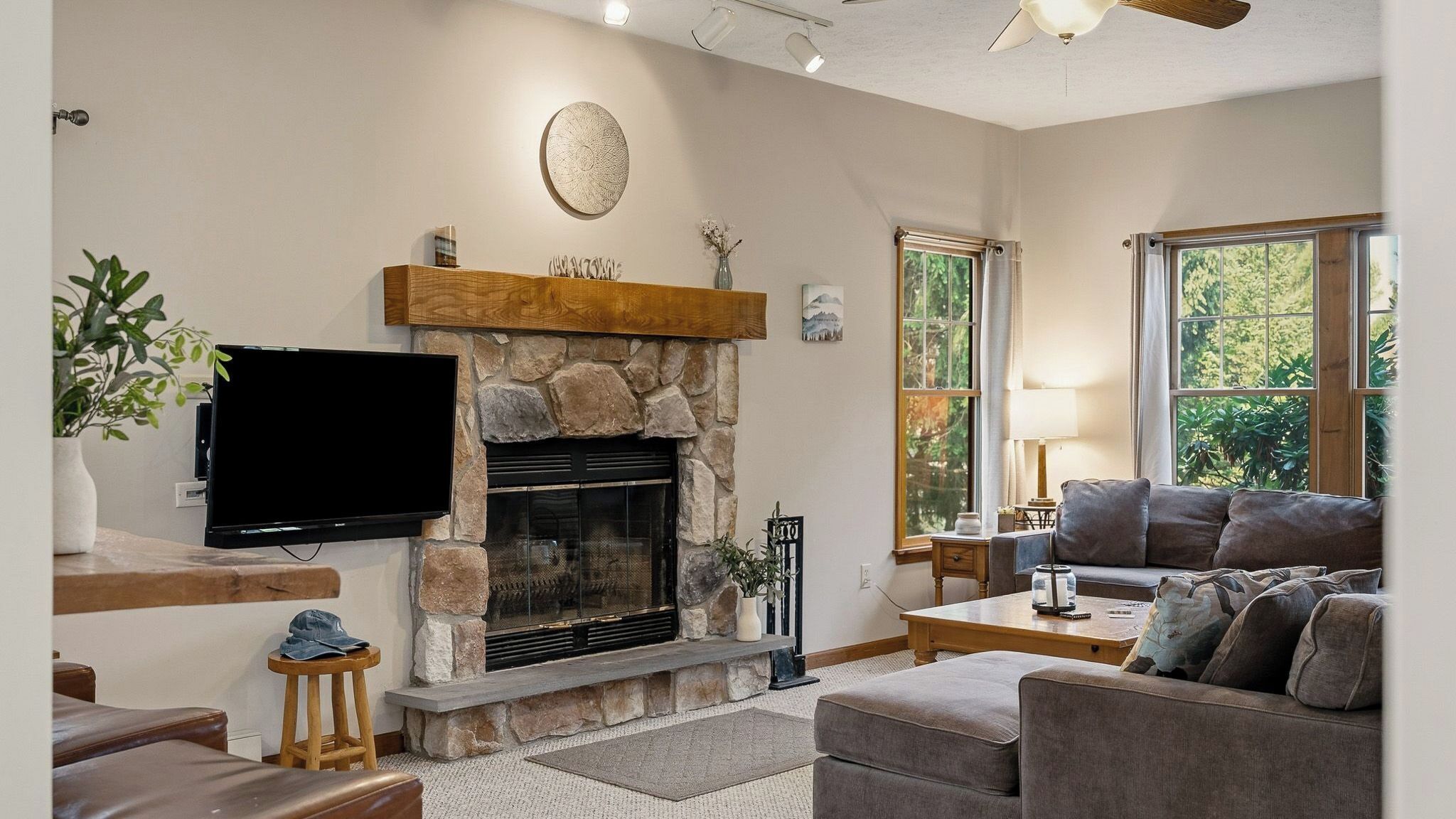 A living room with a stone fireplace, a flat-screen TV, a sofa, and a window with a view of greenery.