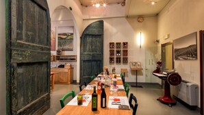 Un'area pranzo con un tavolo lungo apparecchiato per un pasto, una dispensa con bottiglie di vino e una macchina da cucire d'epoca.