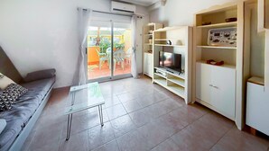 A living room with a sofa, a glass coffee table, a TV on a stand, and a sliding glass door leading to an outdoor area. - Beautiful apartment in Guardamar del Segura with WiFi (Guardamar del Segura)