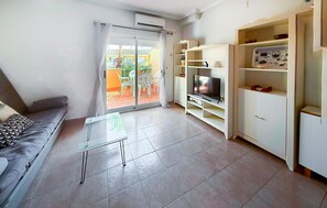 A living room with a sofa, a glass coffee table, a TV on a stand, and a sliding glass door leading to an outdoor area. - Beautiful apartment in Guardamar del Segura with WiFi (Guardamar del Segura)