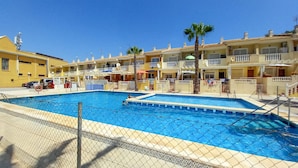 A swimming pool surrounded by a chain-link fence, with a clear blue sky above. - Beautiful apartment in Guardamar del Segura with WiFi (Guardamar del Segura)