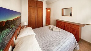 A bedroom with a bed, a nightstand, a painting, a wooden wardrobe, and a mirror on the wall. - Beautiful apartment in Guardamar del Segura with WiFi (Guardamar del Segura)