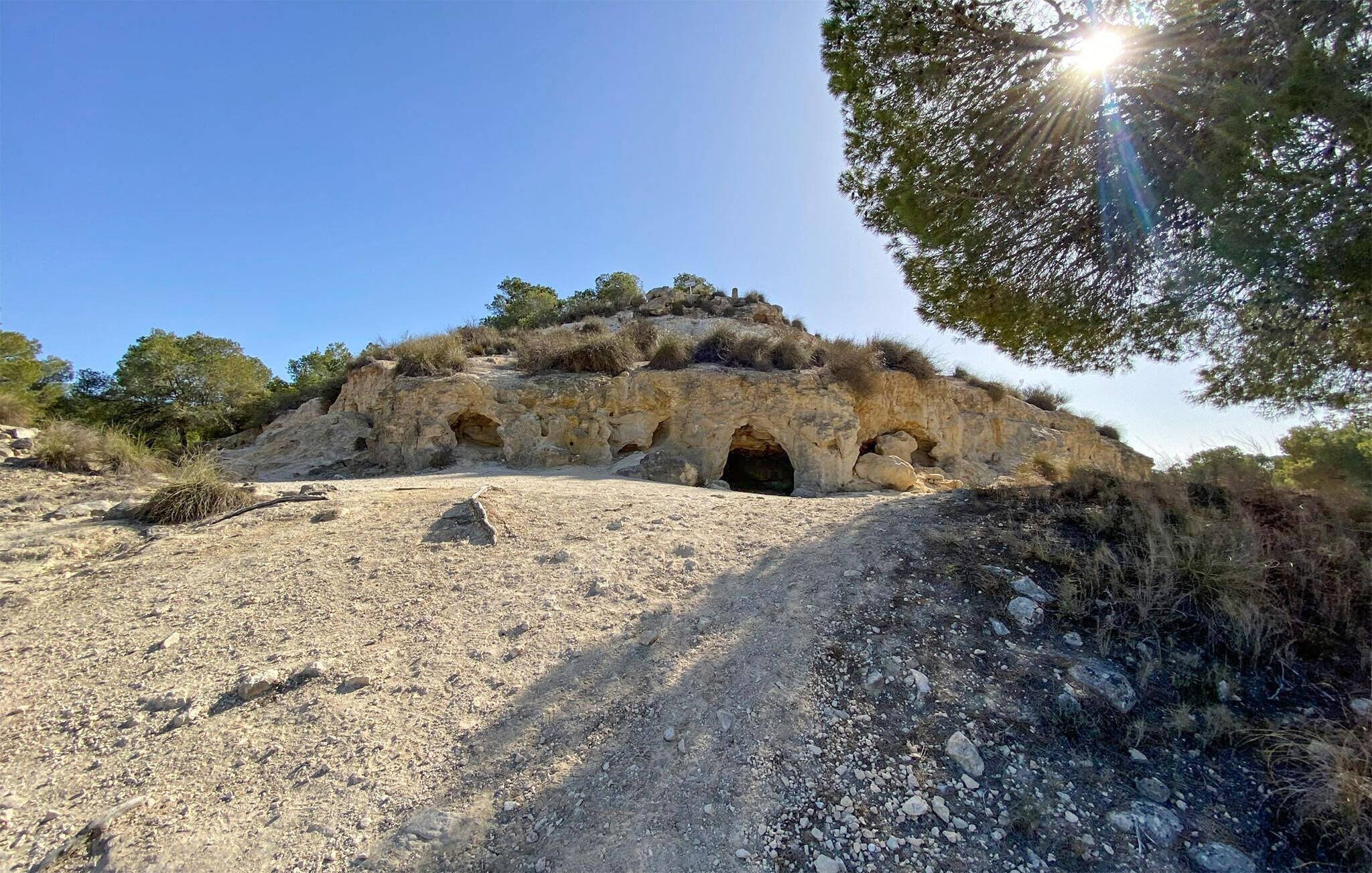 A natural rock formation with caves and sparse vegetation.