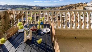 En balkon med et spisebord, der giver udsigt over et naturskønt landskab med bakker og bygninger.