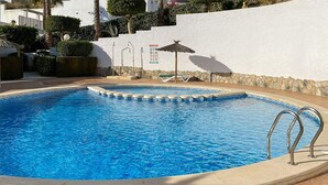 En swimmingpool med stenvæg, liggestol og lille parasol.