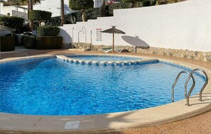 A swimming pool with a stone border, a lounge chair, and a small umbrella. - 2 bedroom awesome apartment in Rojales (Rojales)