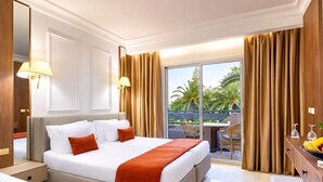 A hotel room with a large bed, a desk, a chair, and a balcony with a view of palm trees. - Résidence Nesrine Cozy Stay in Yasmine  (Port El Kantaoui)