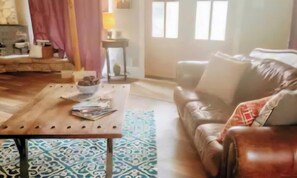 Ein Wohnzimmer mit einer Ledersofa, einem Holztisch und einem gemusterten Teppich.