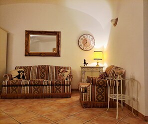 Ein Wohnzimmer mit gemusterten Sofas, einer Wanduhr, einer Lampe und einem Spiegel.