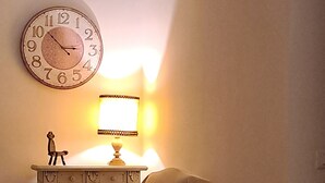 A room with a sofa, a small table with a lamp, a decorative figure, and a wall clock. - Casa Mapi: an oasis of peace in Garbatella, just 3 metro stops from the Colosseum (Roma)