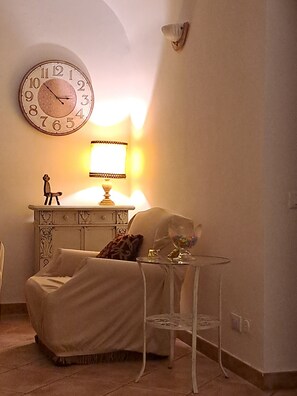 Ein Zimmer mit einer Couch, einem kleinen Tisch mit Lampe, einer Dekofigur und einer Wanduhr.