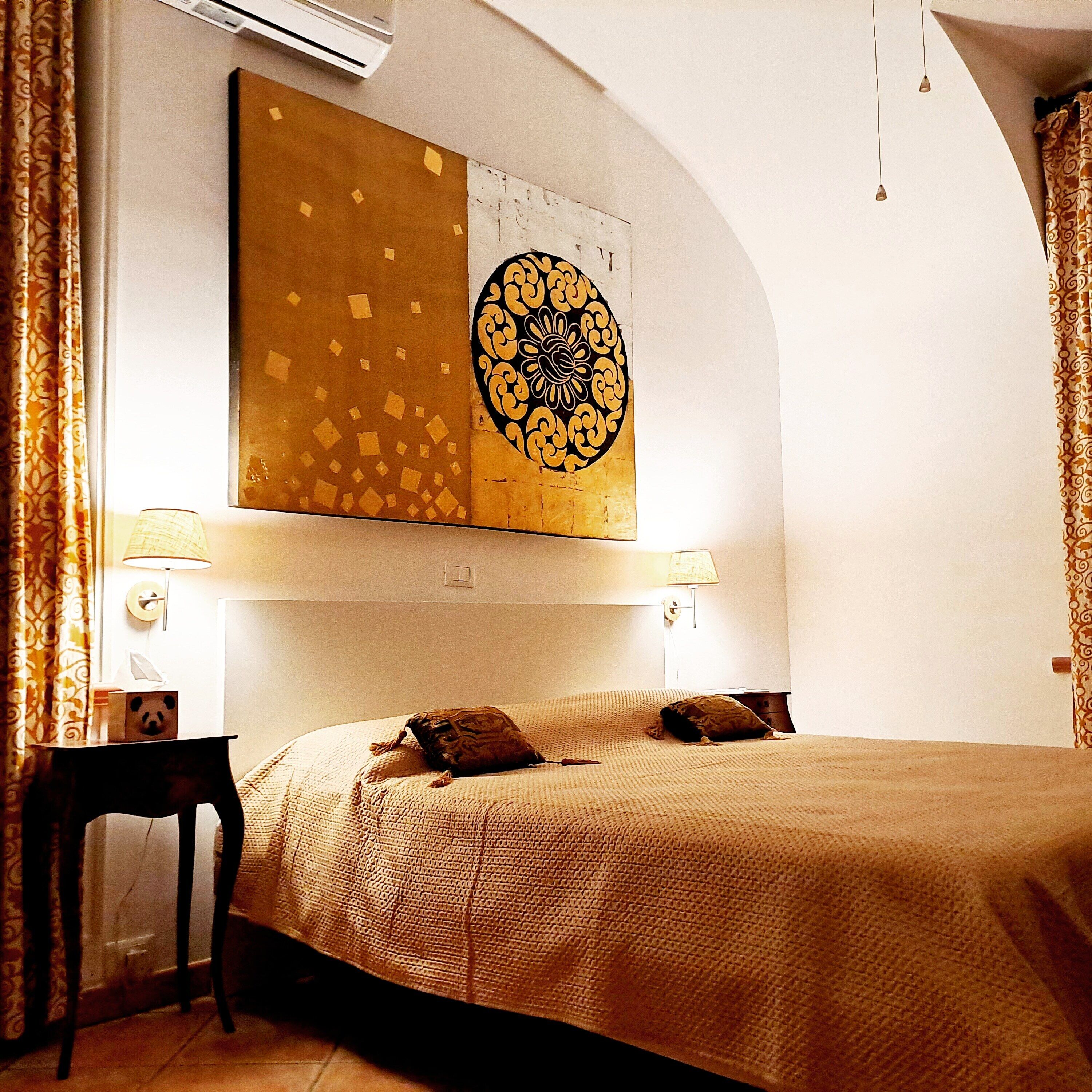 A hotel room with a large bed, two bedside lamps, a wall-mounted air conditioner, and a decorative wall piece.