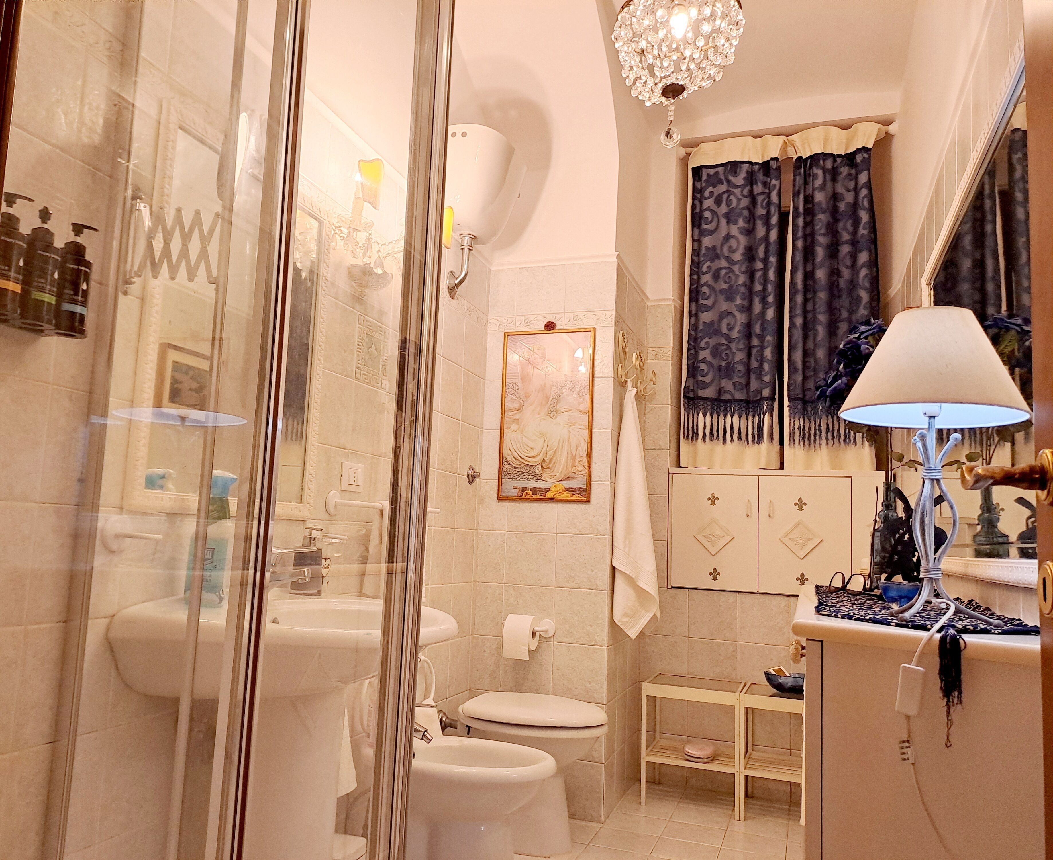 A bathroom with a glass shower enclosure, a sink, a toilet, a vanity with a mirror, and a chandelier.