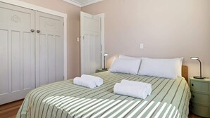 A bedroom with a bed, two bedside tables, a nightstand, and a wardrobe. - Maison Millie - Central, Pet-Friendly, Sleeps 4 (Rotorua)