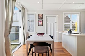 Eine moderne Küche mit Essbereich, ausgestattet mit einem weißen Tisch, schwarzen Stühlen und einem Fenster mit Jalousien.