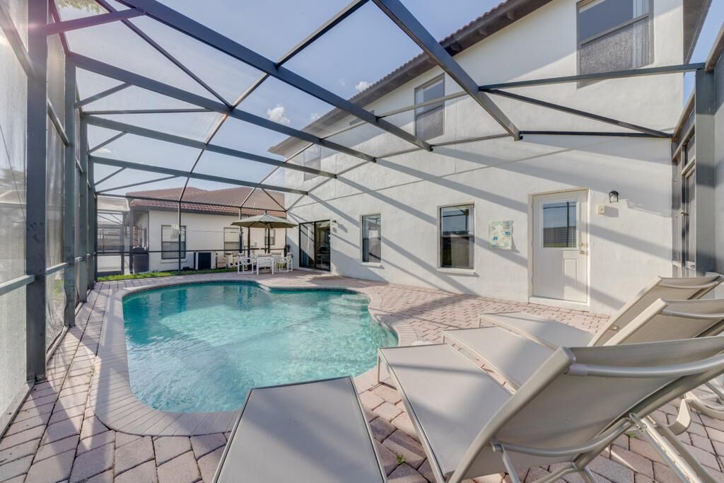 Ein Swimmingpool mit Liegestühlen, einer überdachten Terrasse und einem Haus im Hintergrund.