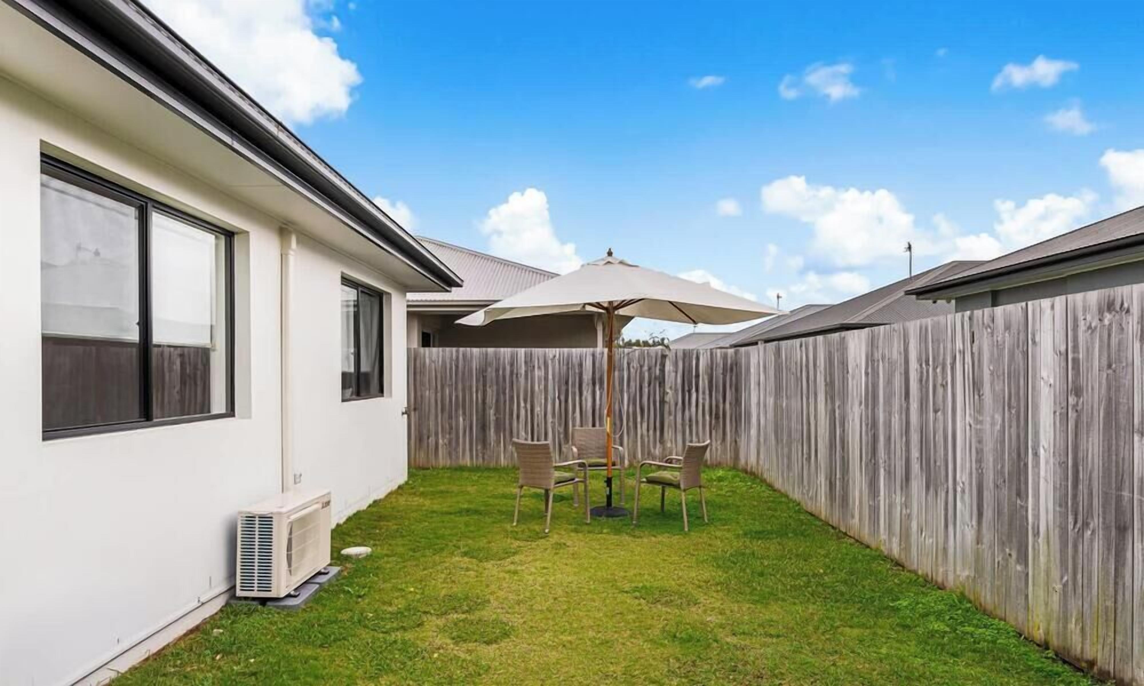 A backyard with a wooden fence, a white house, a table with chairs, and an umbrella.
