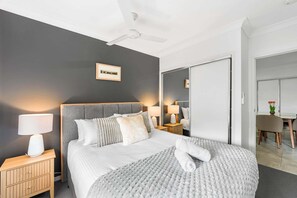 A modern hotel room with a large bed, bedside lamps, a ceiling fan, and a view of the dining area. - Stylish 4BR Sleeps Up To 8 Near Theme Parks (Coomera)