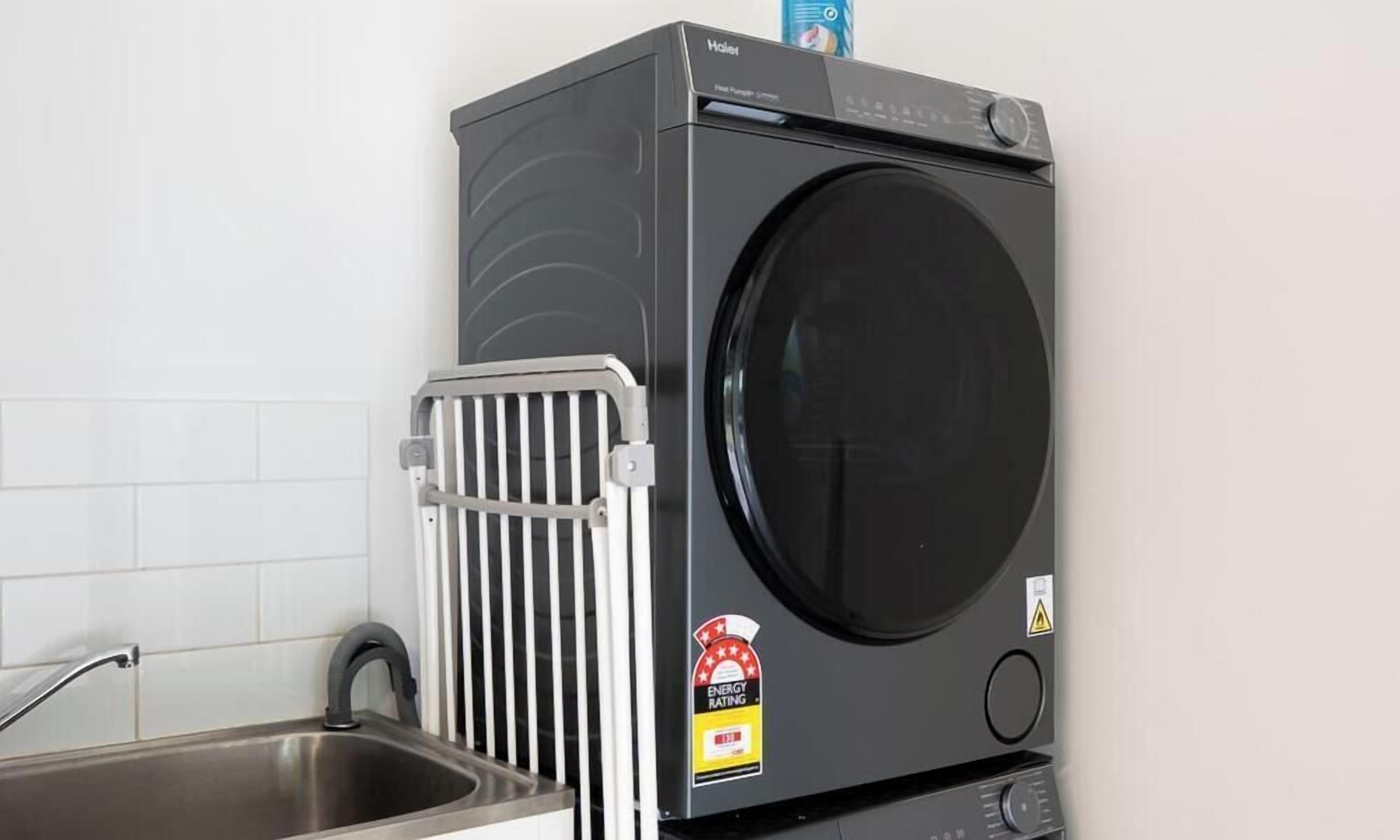 Lavadora compacta y moderna con puerta frontal, ubicada al lado de un lavamanos de acero inoxidable en una cocina.